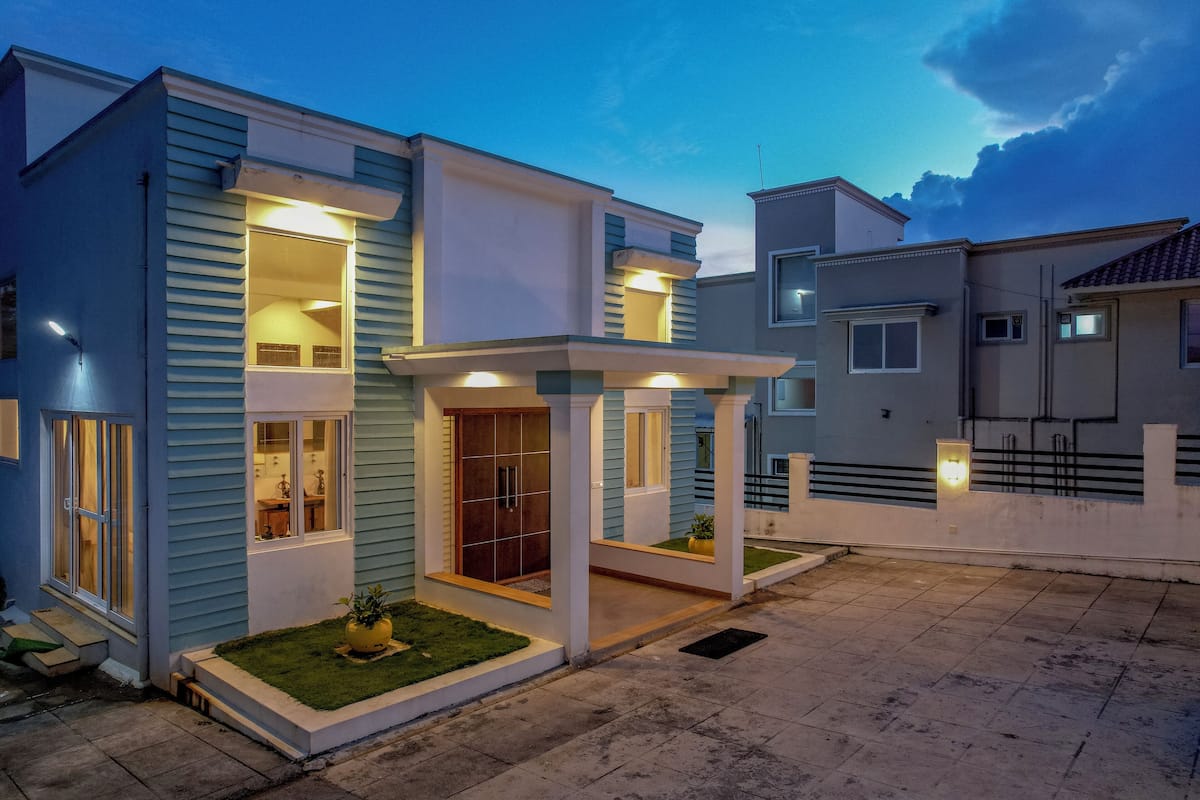 A modern two-story house with a well-lit entrance, a covered porch, and a small garden area.