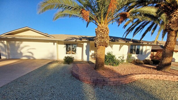 A residential house with a gravel driveway, palm trees, and a brick border. - Suncity west Golf course community (Sun City West)