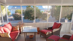A covered patio area with wicker furniture, a tiled floor, and large windows offering views of the outdoors. - Suncity west Golf course community (Sun City West)