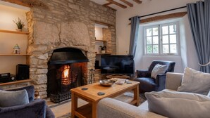 Une cheminée en pierre avec un téléviseur au-dessus, une table en bois et un coin salon confortable avec une fenêtre.
