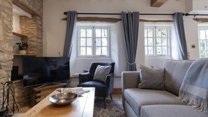 Un salon avec un mur en pierre, des poutres en bois, un téléviseur, un canapé, un fauteuil et une table sur laquelle se trouve un saladier.