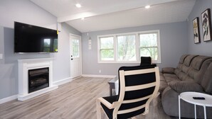 Een woonkamer met een open haard, een televisie, een bank en een fauteuil.