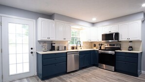 Een moderne keuken met witte en marineblauwe kastjes, roestvrijstalen apparatuur en een licht houten vloer.