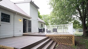 Een huis met een houten terras, een witte schutting en een deur naar een overdekte patio.