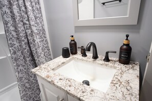 Une salle de bain avec un lavabo en marbre, deux flacons de savon liquide, un distributeur de savon noir et un porte-serviettes.