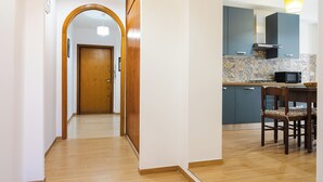 A hallway leading to a kitchen with a wooden door, a dining table with chairs, and a microwave on the counter. - Domus Angelina - Two Bedroom Apartment, Sleeps 4 (Rome)