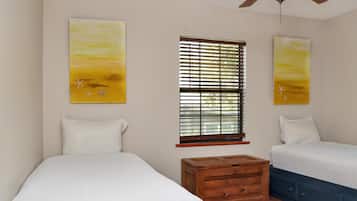 A bedroom with two beds, a ceiling fan, and artwork on the walls.