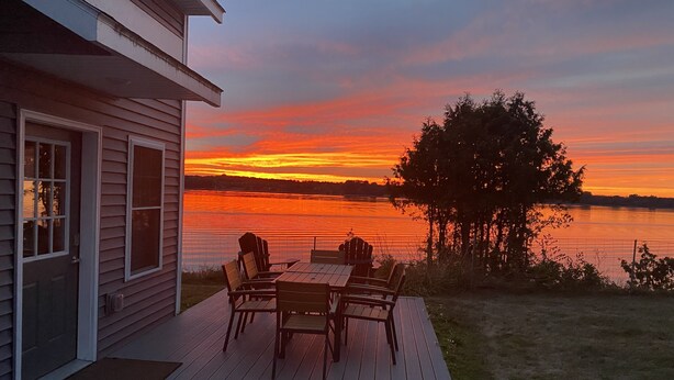 Une terrasse avec une table et des chaises donnant sur un lac au coucher du soleil.