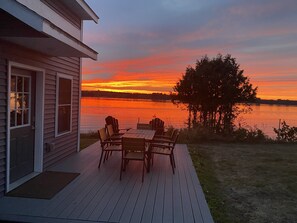 A deck with a table and chairs overlooking a lake at sunset. - #48 Isle View - Sleeps 6, Sunsets & Beach (Alburgh)
