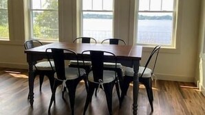 Un espace repas comprenant une table et des chaises, ainsi que de grandes fenêtres donnant sur un plan d’eau.
