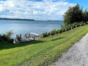 A grassy area with a wooden dock leading to a body of water, a gravel path, and a row of trees. - #48 Isle View - Sleeps 6, Sunsets & Beach (Alburgh)