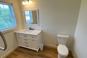 A bathroom with a white vanity, a mirror, a toilet, and a window. - #48 Isle View - Sleeps 6, Sunsets & Beach (Alburgh)