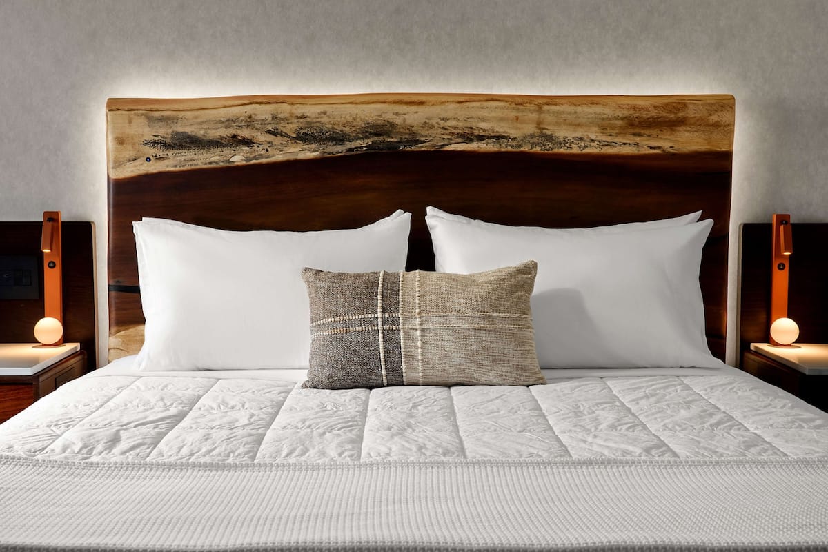 A bed with a wooden headboard, white bedding, and two bedside lamps.