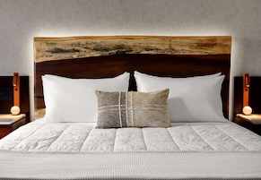 Una cama con cabecera de madera, ropa de cama blanca y dos lámparas de noche.