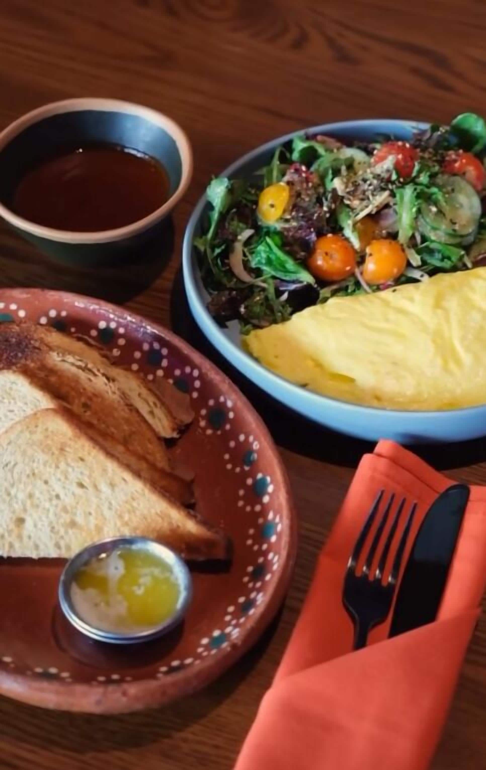 A plate with toast, a small bowl of butter, and a salad with cherry tomatoes.