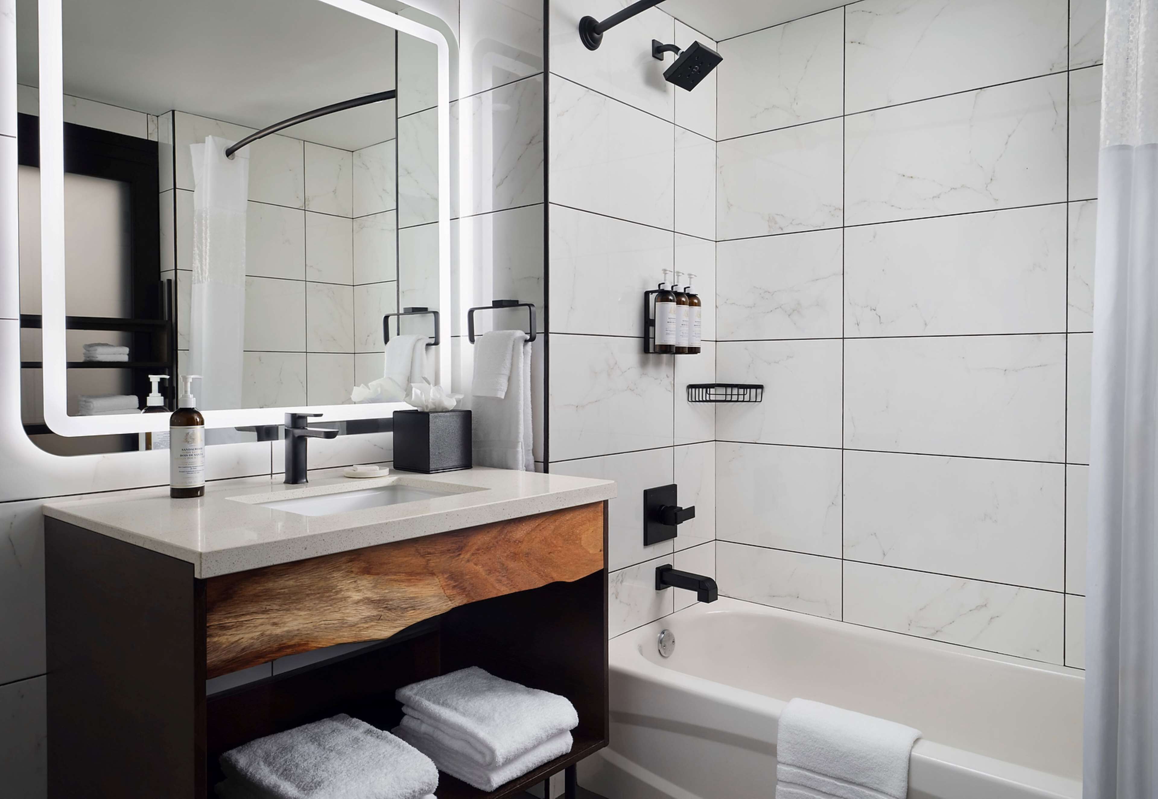 A modern bathroom with a large mirror, two sinks, a bathtub, and a shower.