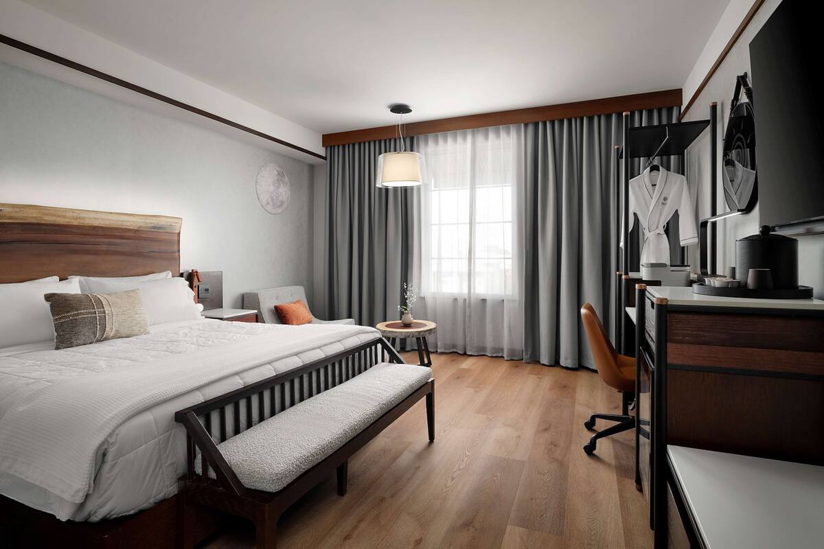 A modern hotel room with a large bed, a bench, a desk, and a chair.