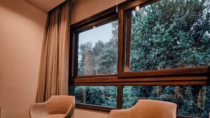 A modern room with two armchairs and a small table, large windows with a view of trees, wooden flooring, and a ceiling light. - Hotel Tre (Puerto Iguazú)