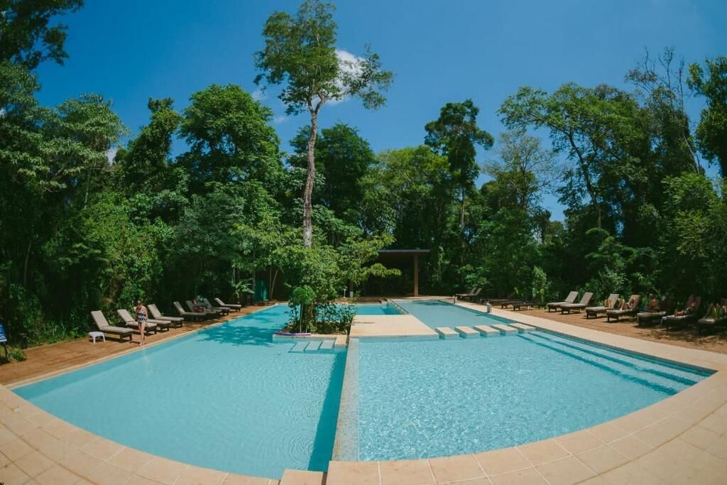Una piscina con sillas de descanso y una pérgola rodeada de árboles.
