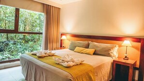A neatly made bed with a yellow throw blanket, two bedside lamps, and a view of greenery through a window. - Hotel Tre (Puerto Iguazú)