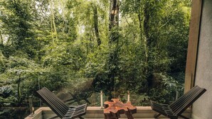 A modern outdoor seating area with two chairs and a wooden table, overlooking a lush, green forest. - Hotel Tre (Puerto Iguazú)