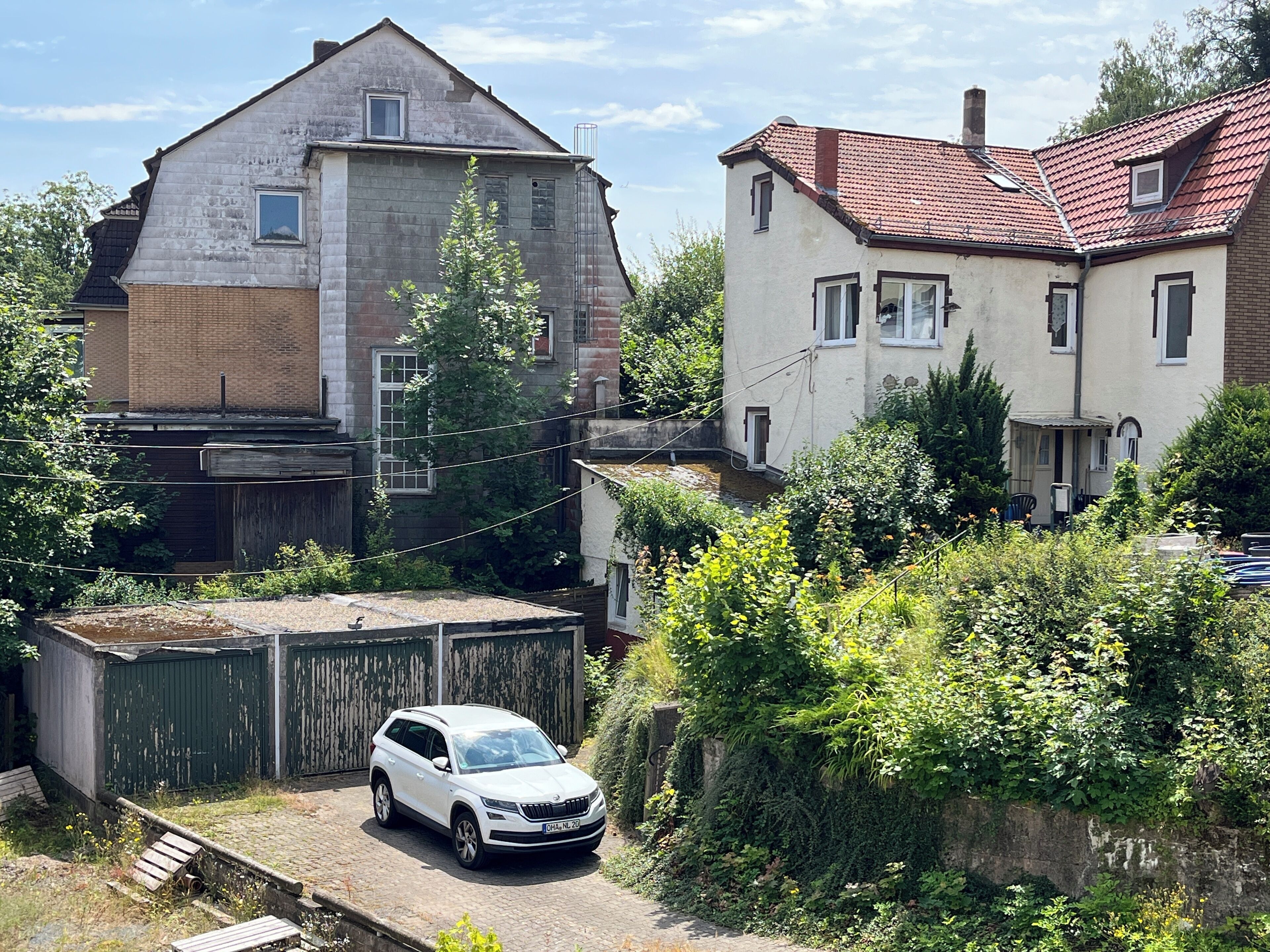 Ein Wohngebiet mit einem weißen SUV vor einem Haus mit geneigtem Dach und einer Ziegelhausfassade.
