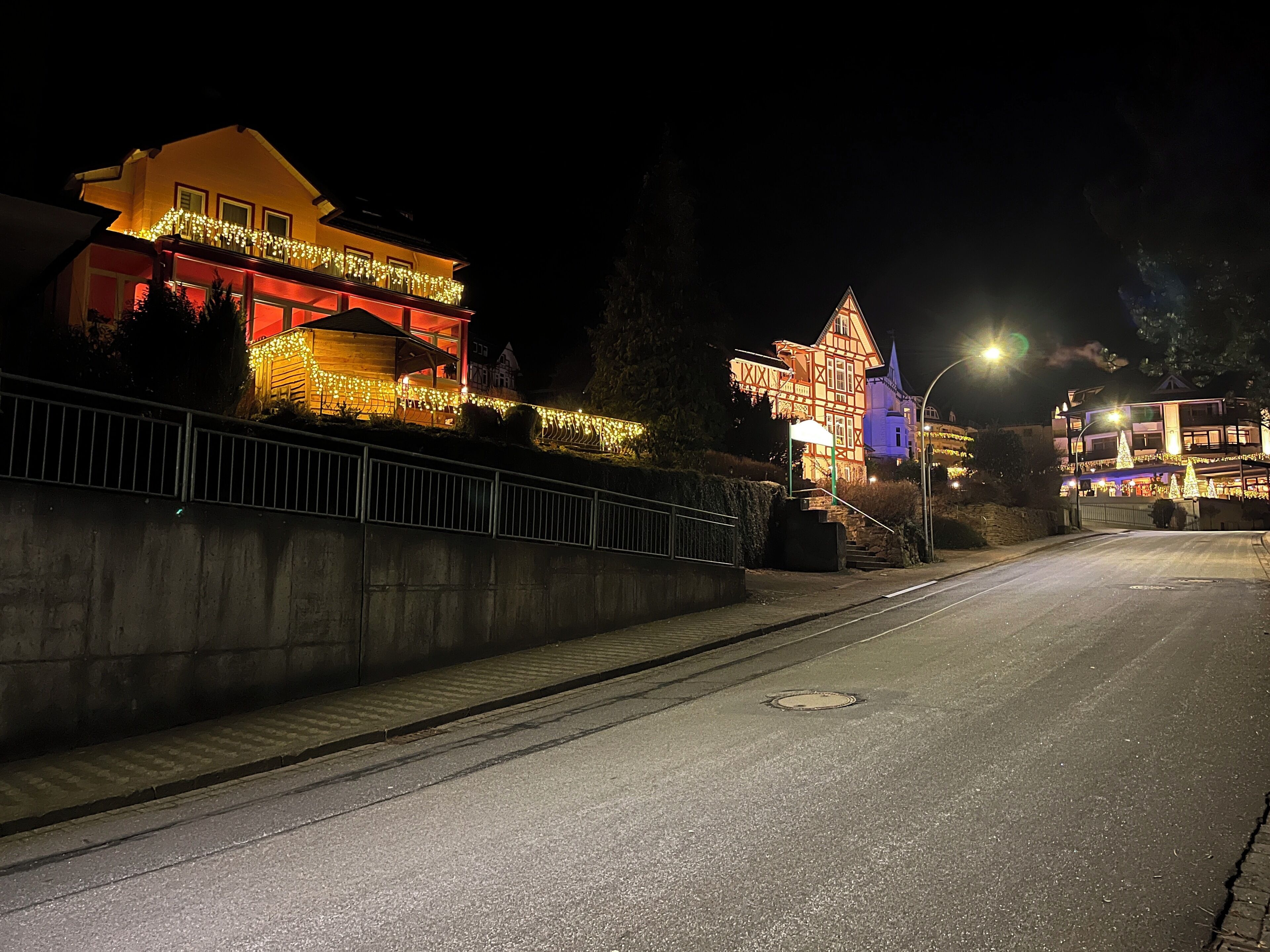 A street at night with a brightly lit house on the left and a lit-up building on the right.