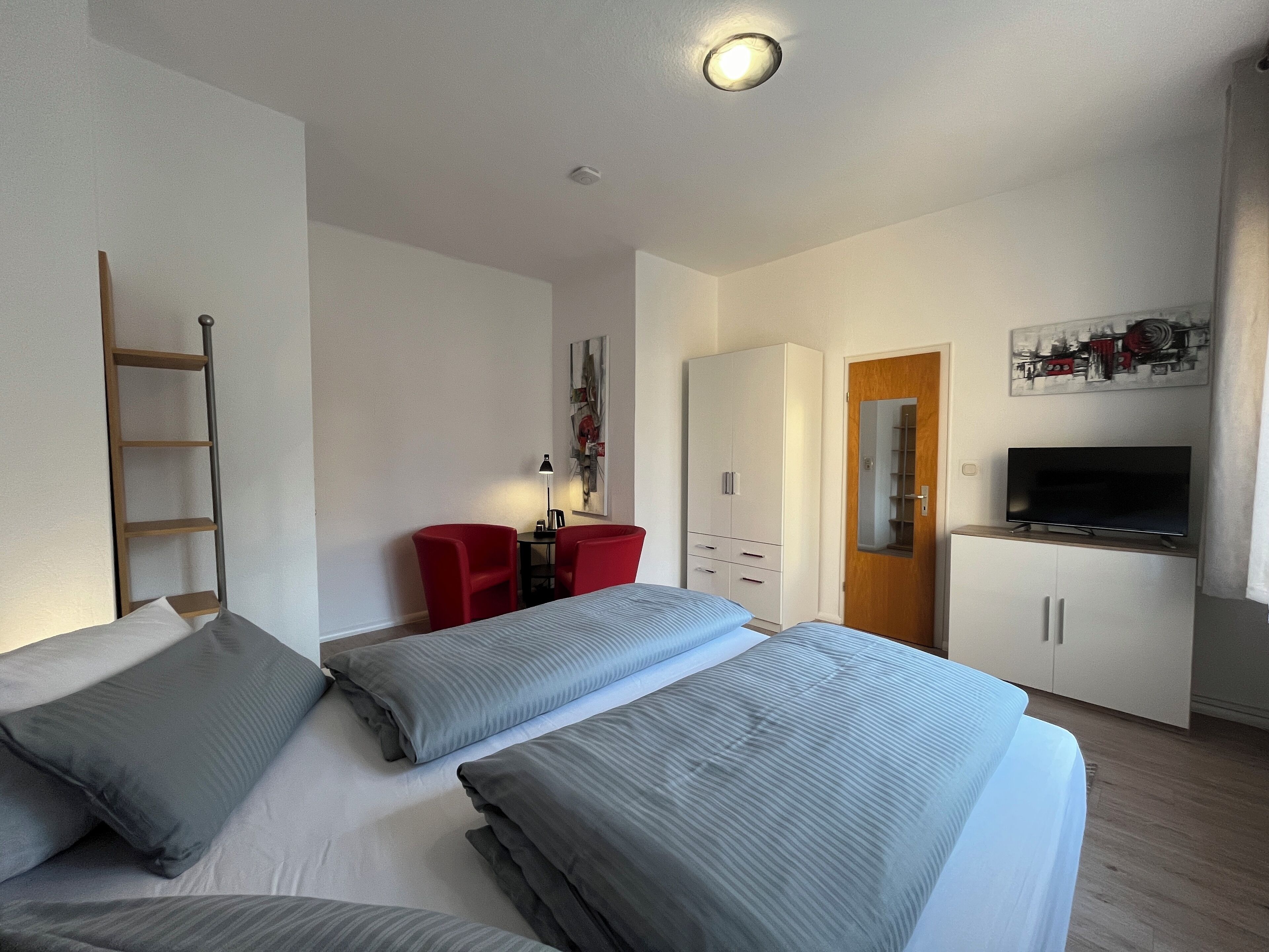 Hotelkamer met een bed, twee rode stoelen, een bureau met lamp, een kledingkast en een televisie.