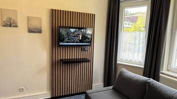 Ein modernes Wohnzimmer mit einem Wandfernseher, einer Couch und einem Fenster mit Vorhängen.