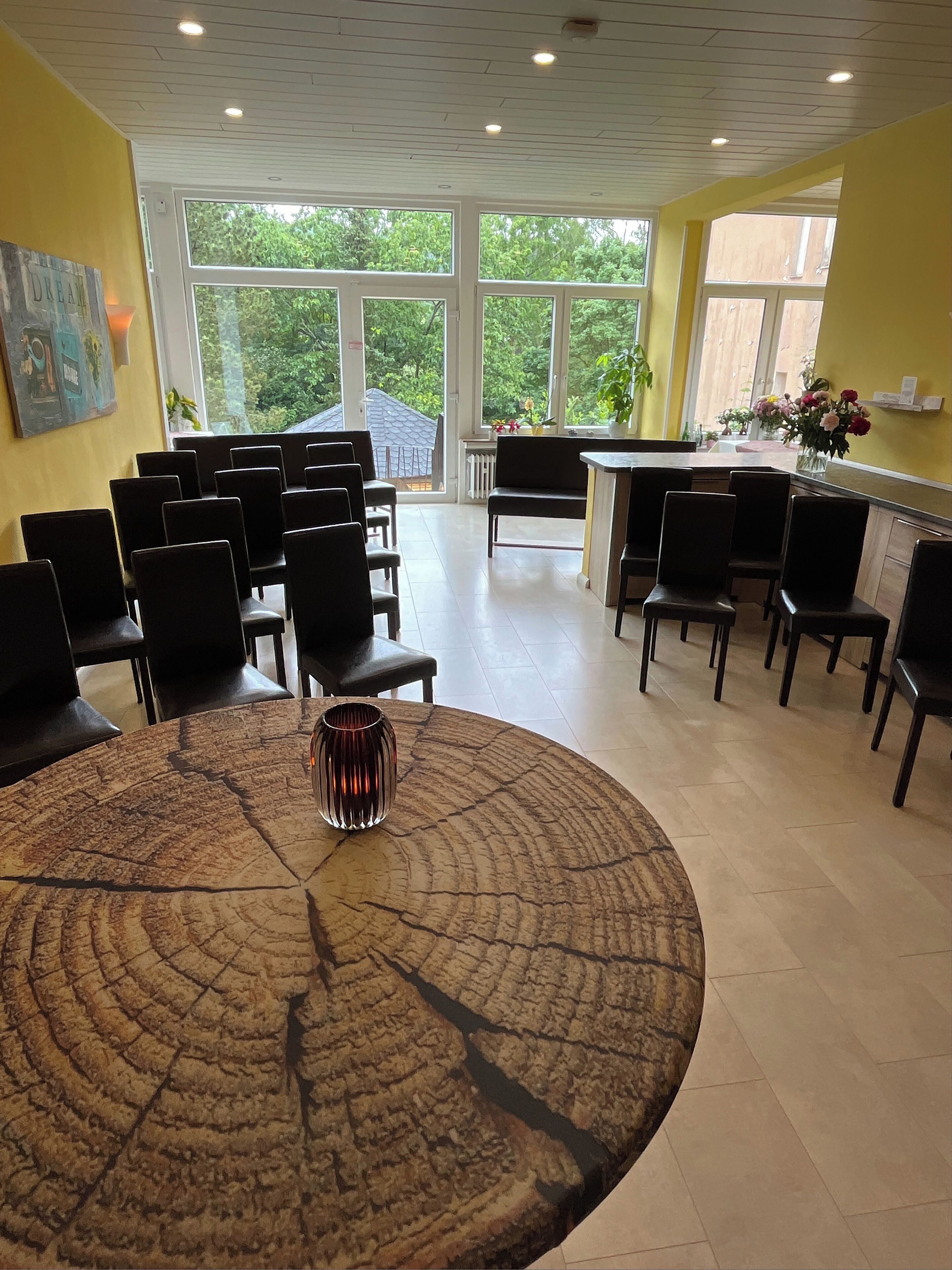 Ein Konferenzraum mit einem großen runden Tisch, mehreren Stühlen und Blick auf Grünflächen durch große Fenster.