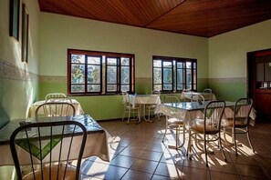 Un comedor con mesas y sillas, ventanas amplias y piso de baldosas.