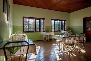 A dining area with tables and chairs, large windows, and a tiled floor.