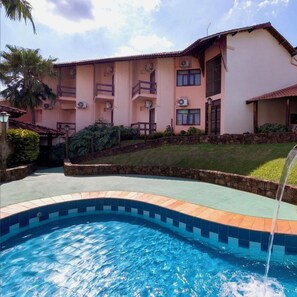 A hotel with a swimming pool, a stone wall, and a well-maintained lawn.
