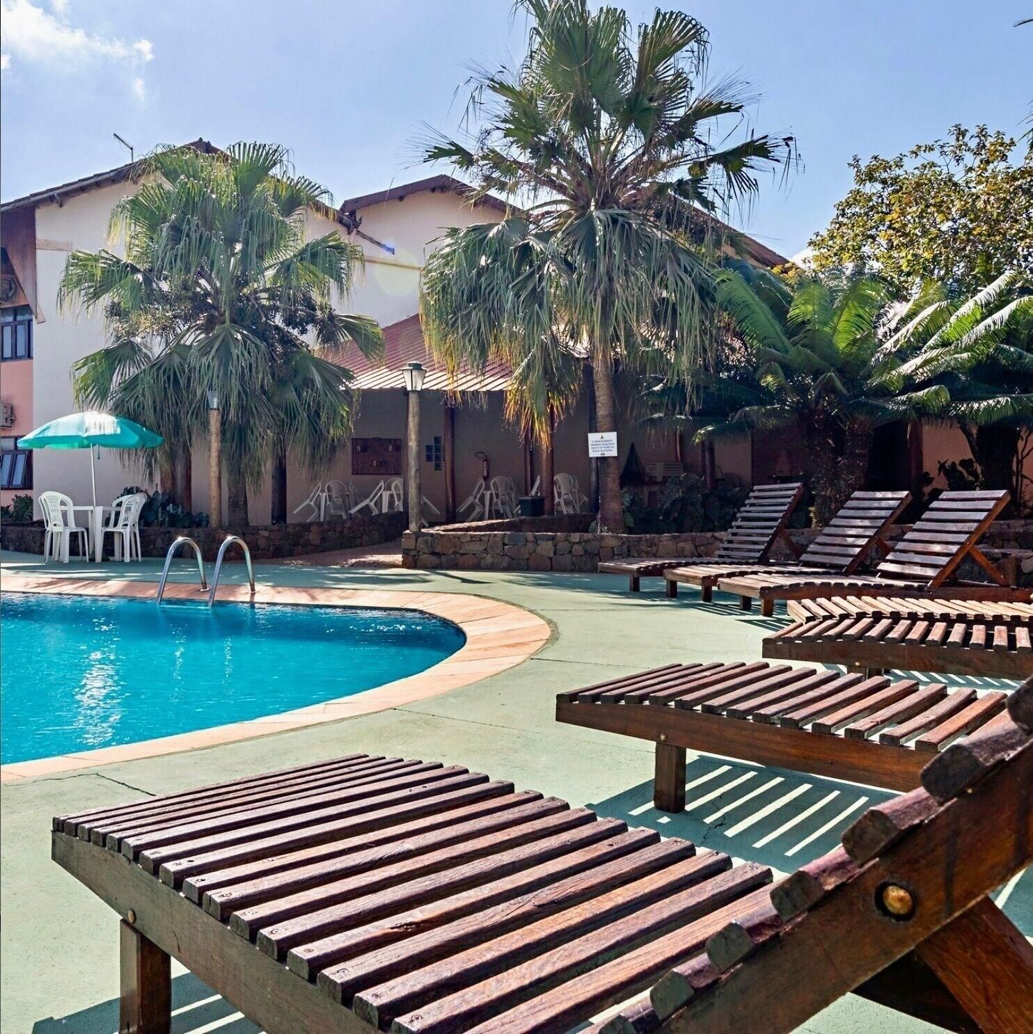 A pool area with lounge chairs, a swimming pool, palm trees, and a building in the background.