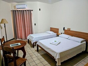 Una habitación de hotel con dos camas individuales, una mesa con sillas, una lámpara y una cortina.