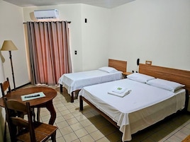 A hotel room with two single beds, a table with chairs, a lamp, and a curtain.