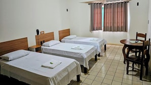 Una camera d'albergo con due letti singoli, un tavolino con una sedia, una finestra con tende e pavimento piastrellato.