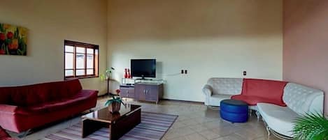 A spacious living room with a red sofa, a white sofa, a blue ottoman, a television, and a cabinet.