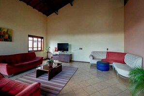 Un salón espacioso con un sofá rojo, un sofá blanco, un reposapiés azul, un televisor y un armario.