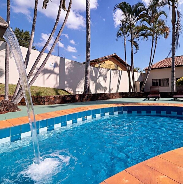 Piscina con fuente, rodeada de palmeras y un muro de piedra.