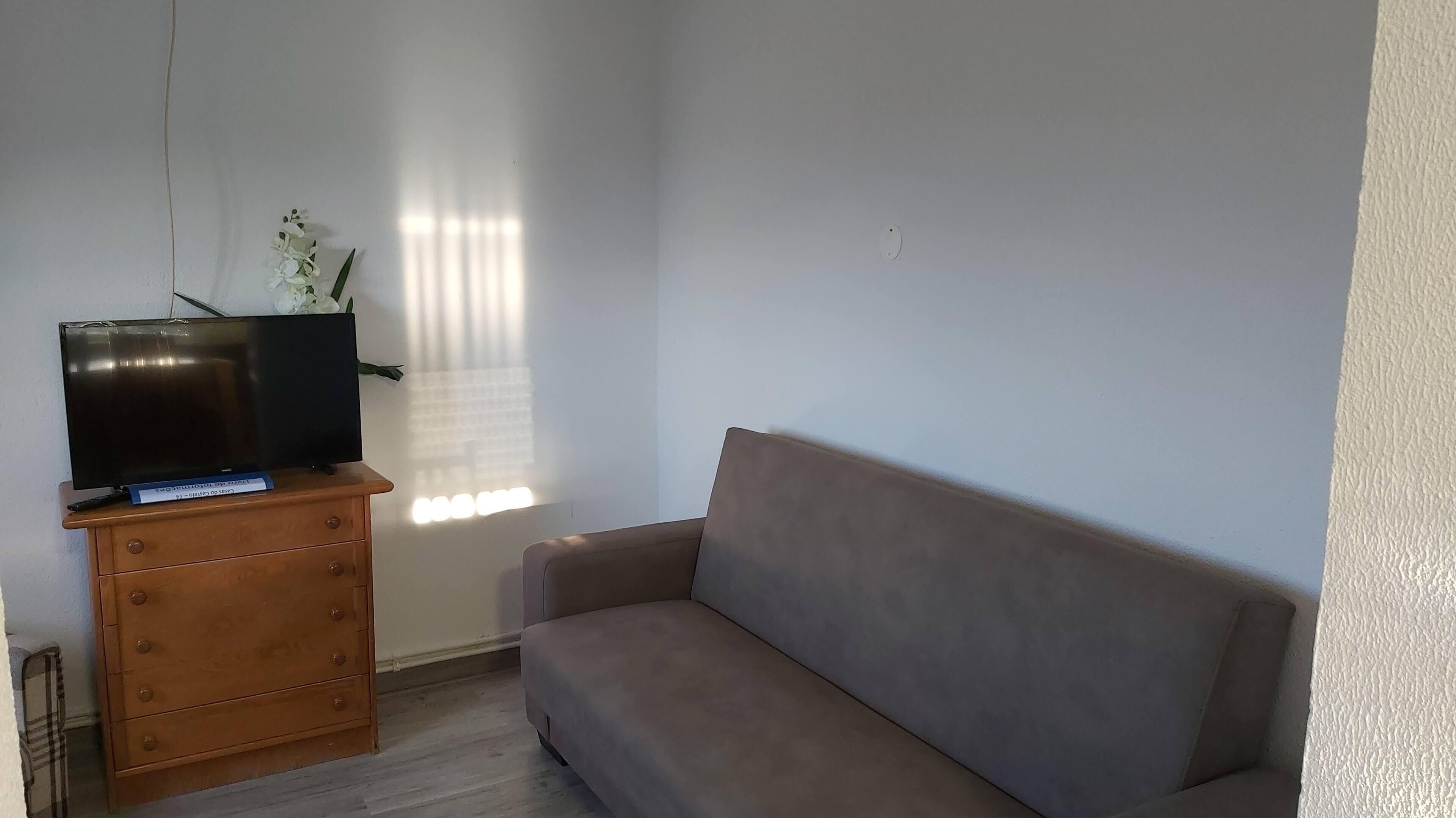 A living room with a flat-screen TV on a wooden cabinet, a beige sofa, and a window with blinds.