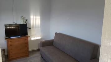A living room with a flat-screen TV on a wooden cabinet, a beige sofa, and a window with blinds.