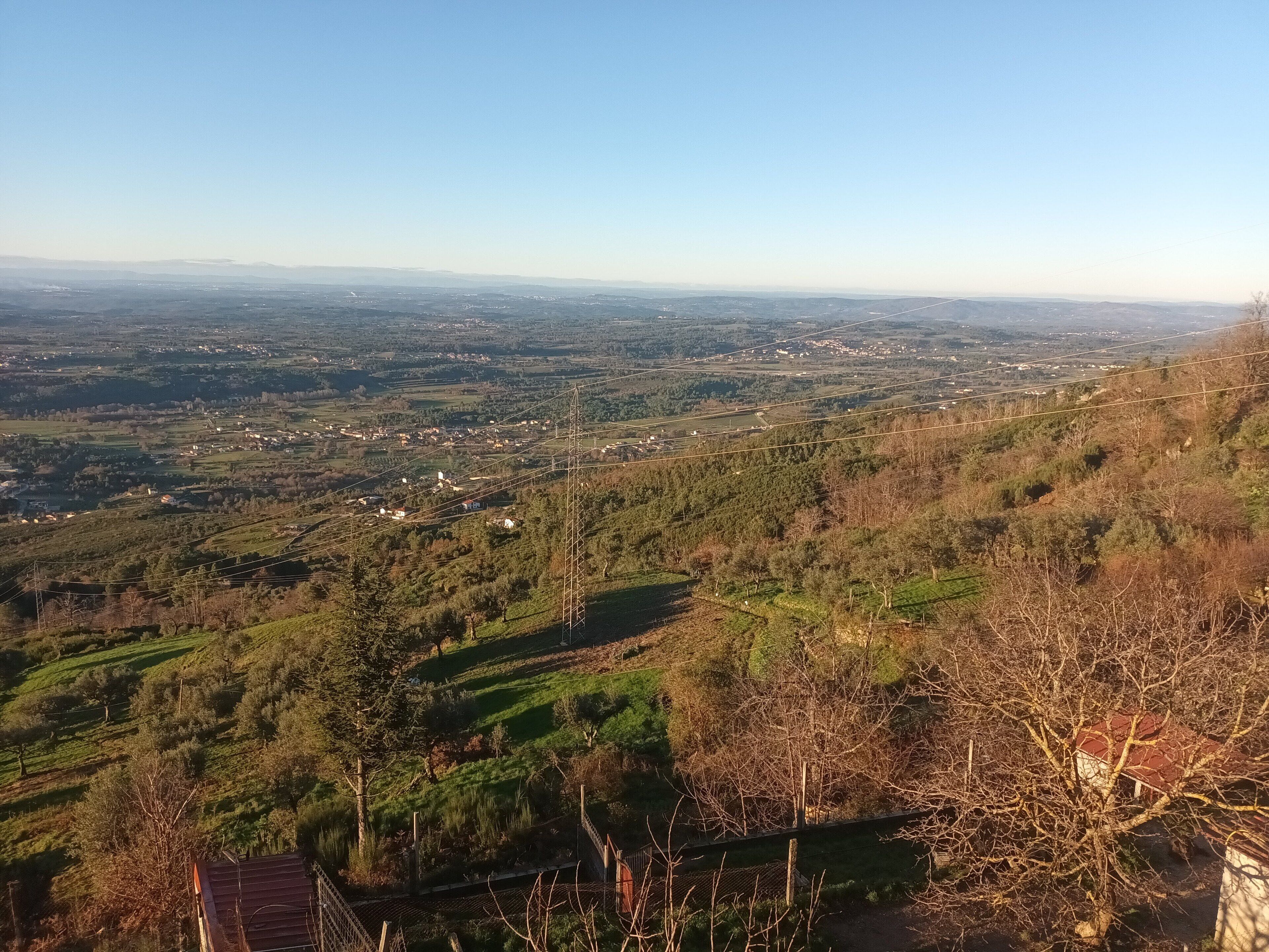 A panoramic view of a hilly landscape with scattered buildings and a power line tower.