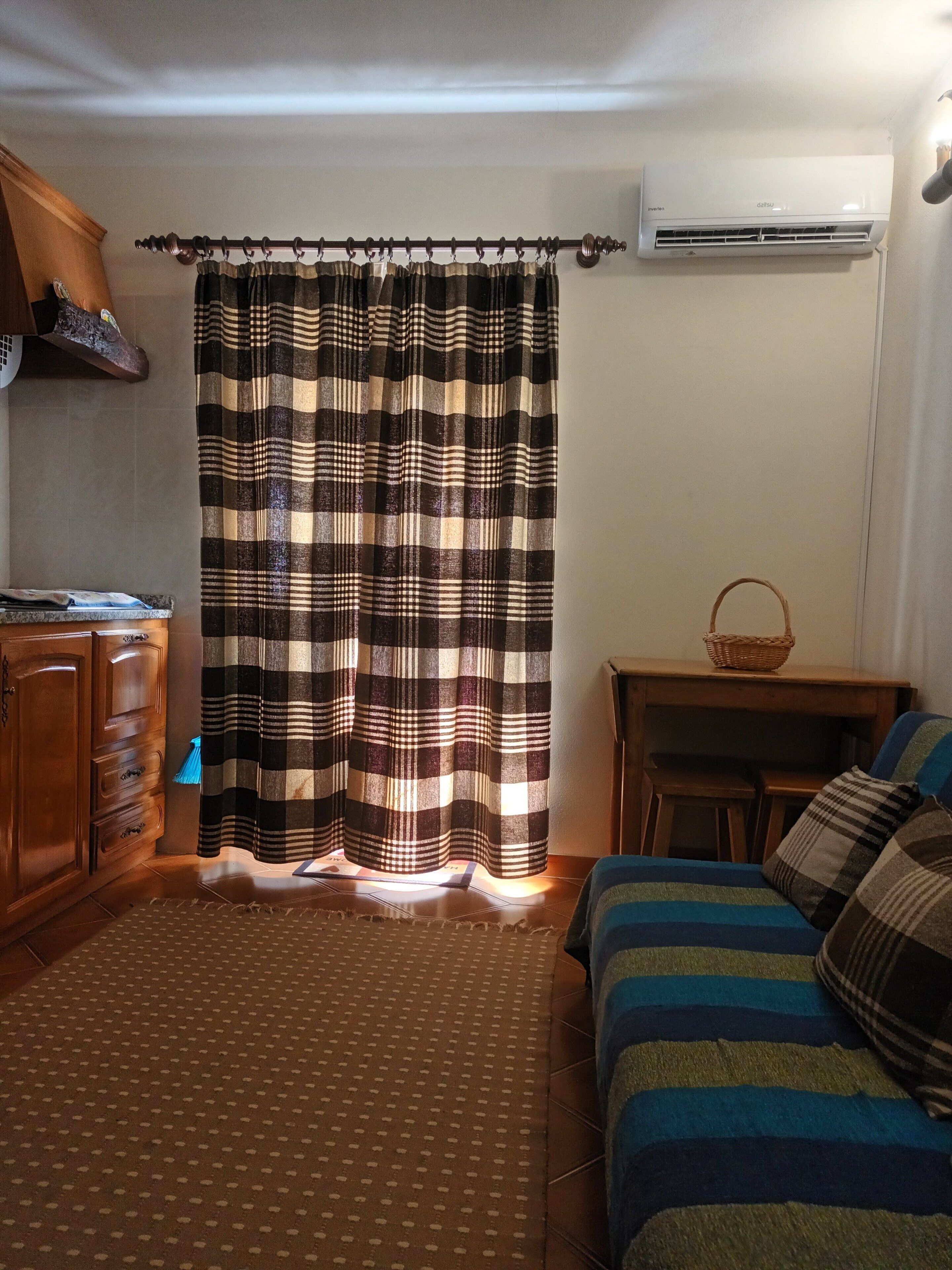 Una camera da letto con tenda a quadretti, un armadio in legno, un tavolino con un cesto e un letto con lenzuola a righe.