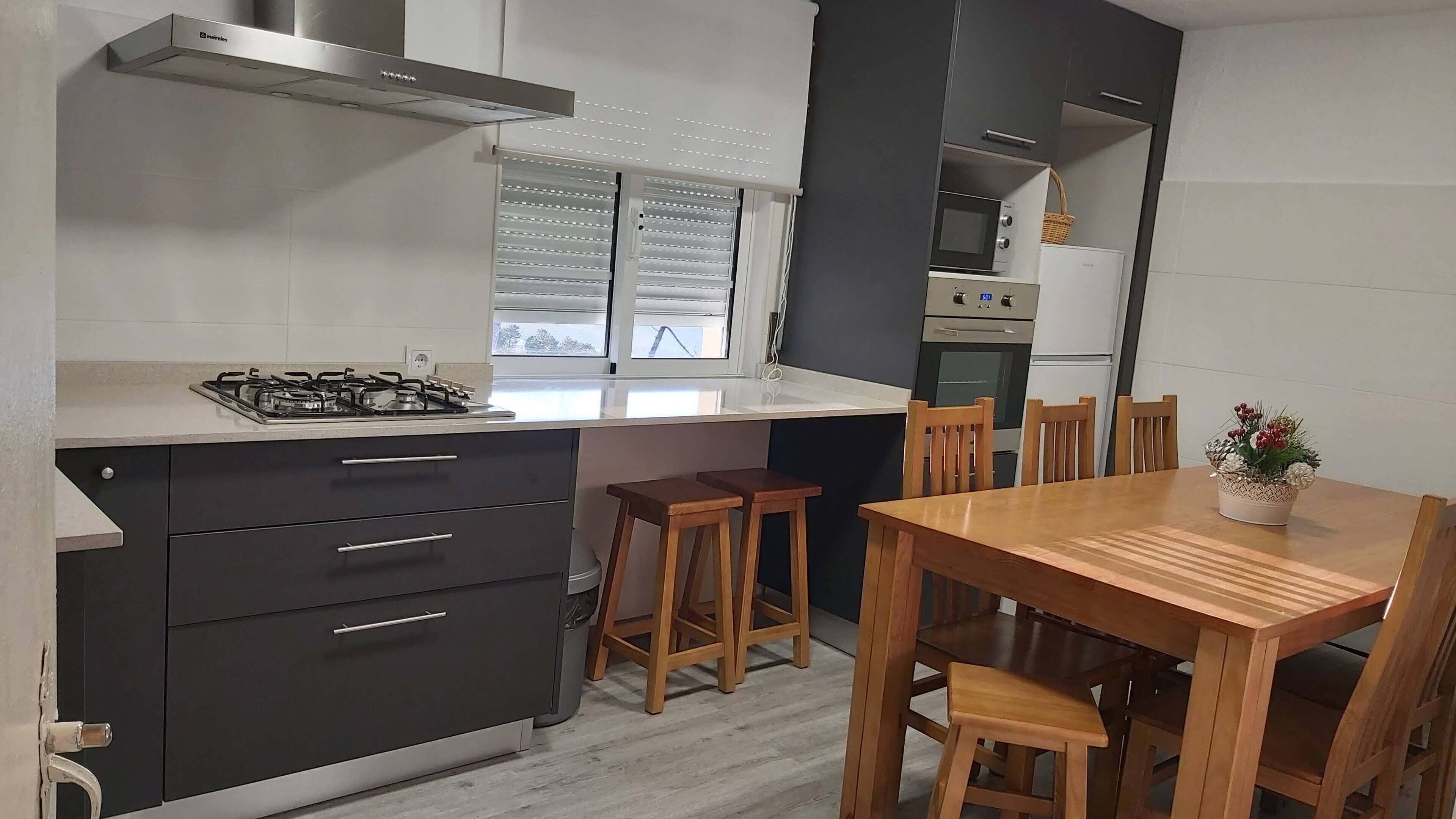 Een moderne keuken met een gasfornuis, donkere kastjes en een eethoek met houten stoelen en een tafel.