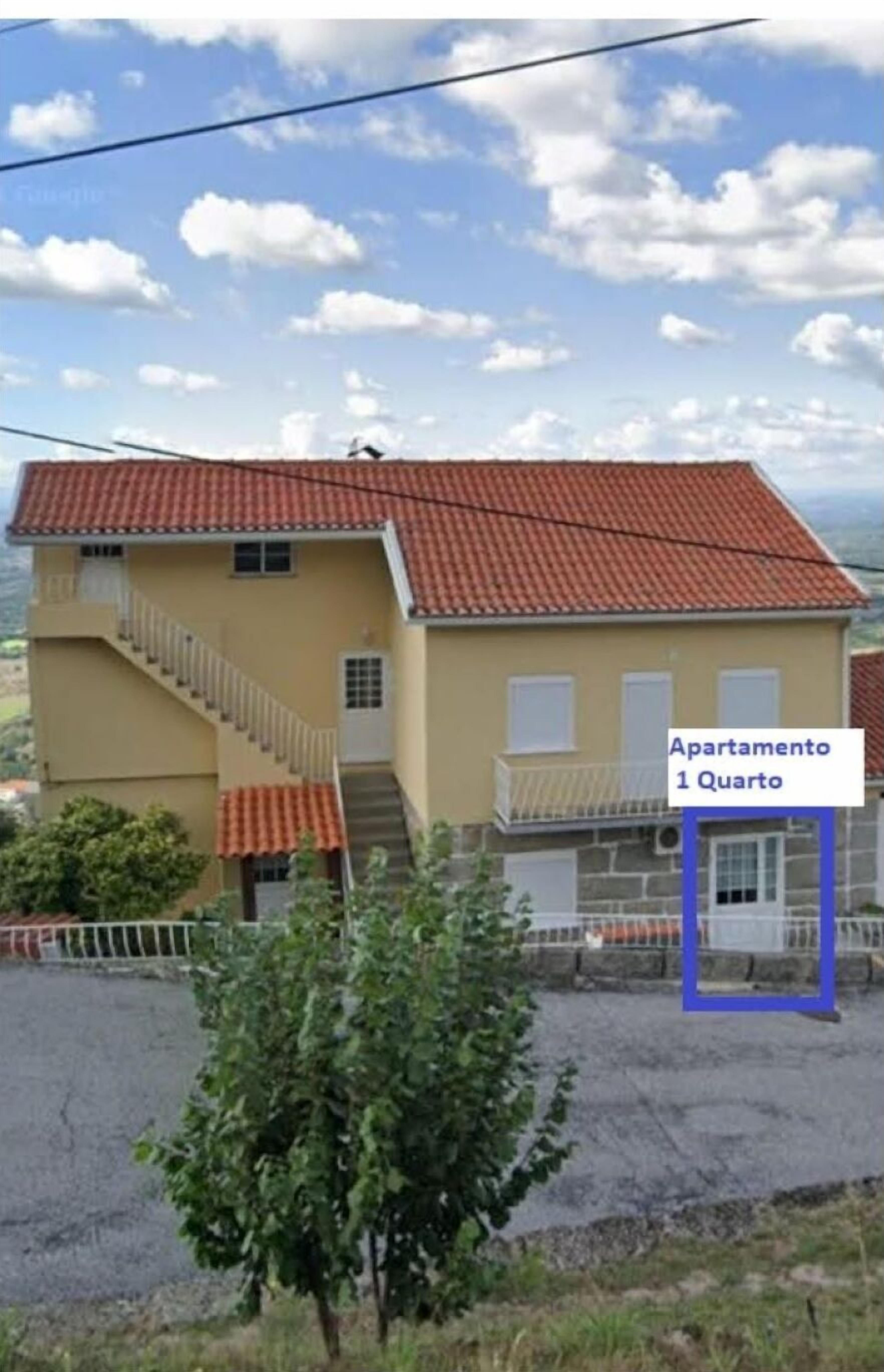 A two-story building with a red-tiled roof and a balcony. A sign indicates it is an apartment on the first floor.
