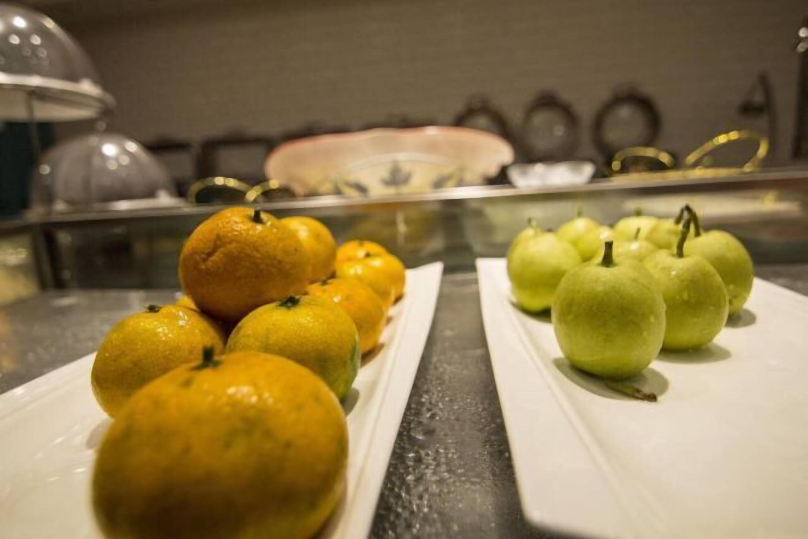 Een buffettafel met schalen vol sinaasappels en groene appels.