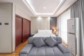 A modern hotel room with a large bed, a seating area with cushions, a wardrobe, a desk with a lamp, and a refrigerator. - Westcare Hotel (Century City New Convention and Exhibition Center Tianfu 3rd Street Store) (Chengdu)