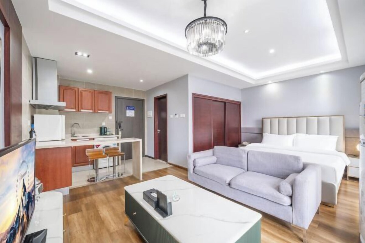 A modern hotel room with a sofa, a bed, a dining area, and a kitchen.