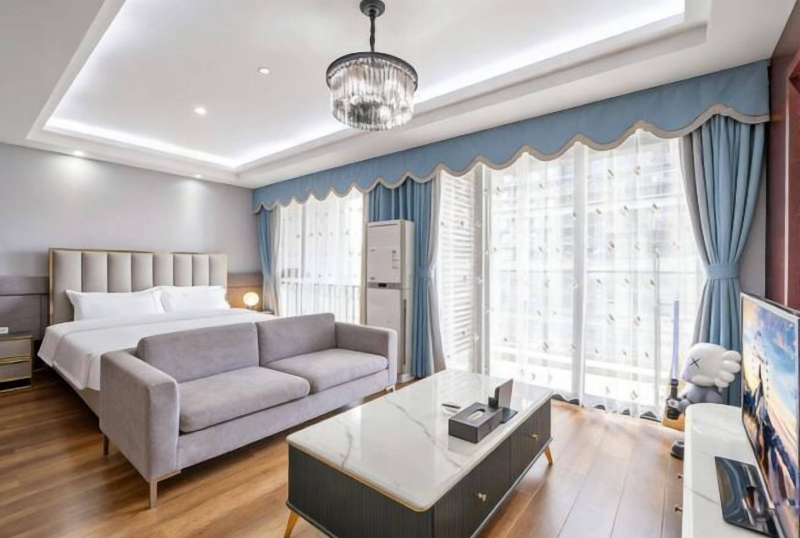 Una habitación de hotel moderna con cama, sofá, escritorio y ventanas grandes con cortinas.